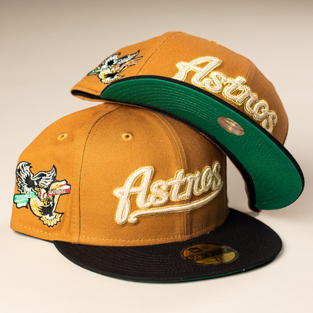 Two El Gallo Canvas Bronze Black Houston Astros 5950 Fitted New Era Hats: both mustard-yellow with black brims, green underbrims, and embroidered logos; one is upright showing the front, the other tilted to show the underside and side patch.
