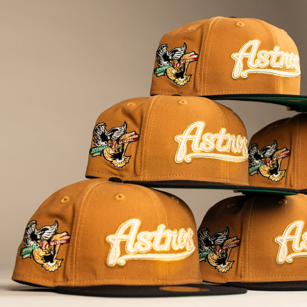 Multiple El Gallo Canvas Bronze Black Houston Astros New Era 5950 Fitted hats are stacked, each featuring a bird and "Astros" script embroidered on the front, with multicolored details on the side.