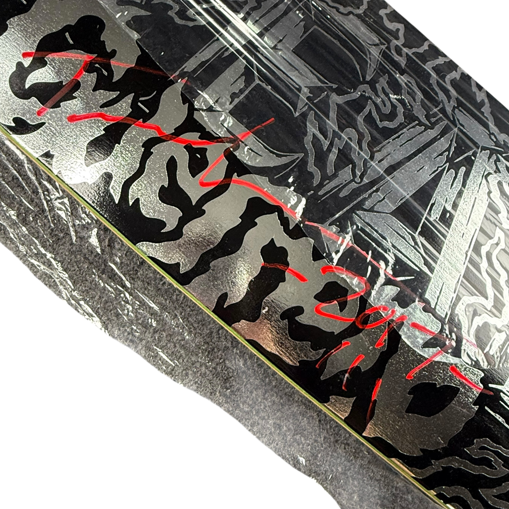 A close-up of a signed Tommy Guererro Silver Black Real Skateboards Deck 9x31.4 Circa 2017 Collectible, featuring stylized black and silver graphics with bold red handwritten text, resting on a gray surface.