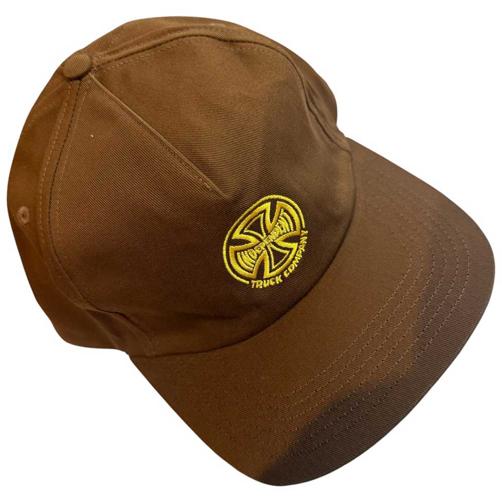 The Truck Co Legacy Brown Hat is an unstructured tan snapback with a low-profile fit, featuring a yellow embroidered circular logo and "Truck Company" text on the front. Unisex, by Independent Skateboards.
