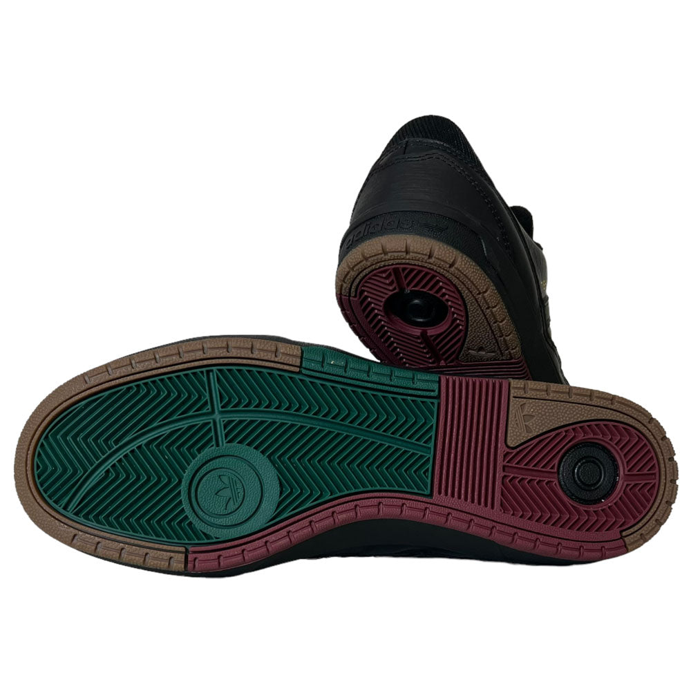 A pair of Tyshawn 2 II Adidas Skateboarding Core Black/Core Green Leather Shoes is shown—one upright, one tilted to reveal the sole featuring green, brown, and maroon sections with textured patterns and circular details.