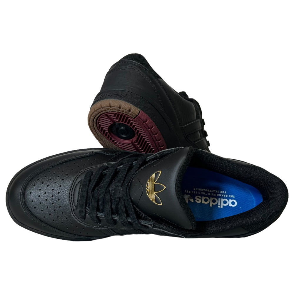 A pair of Tyshawn 2 II Adidas Skateboarding Core Black/Core Green leather shoes with perforated toe details, gold Adidas logo on the tongue, blue insoles, and brown outsoles. One stands upright while the other lies on its side.
