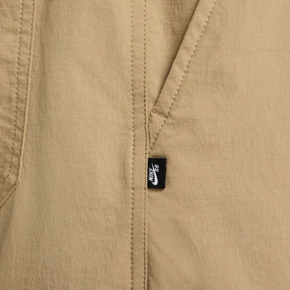 Close-up of FV7347297 Kearny Cargo Pant Khaki Nike SB Skate Dri Fit fabric with a diagonal seam and pocket, featuring a small black tag with white Nike SB logo, highlighting this classic cargo skate pant style.