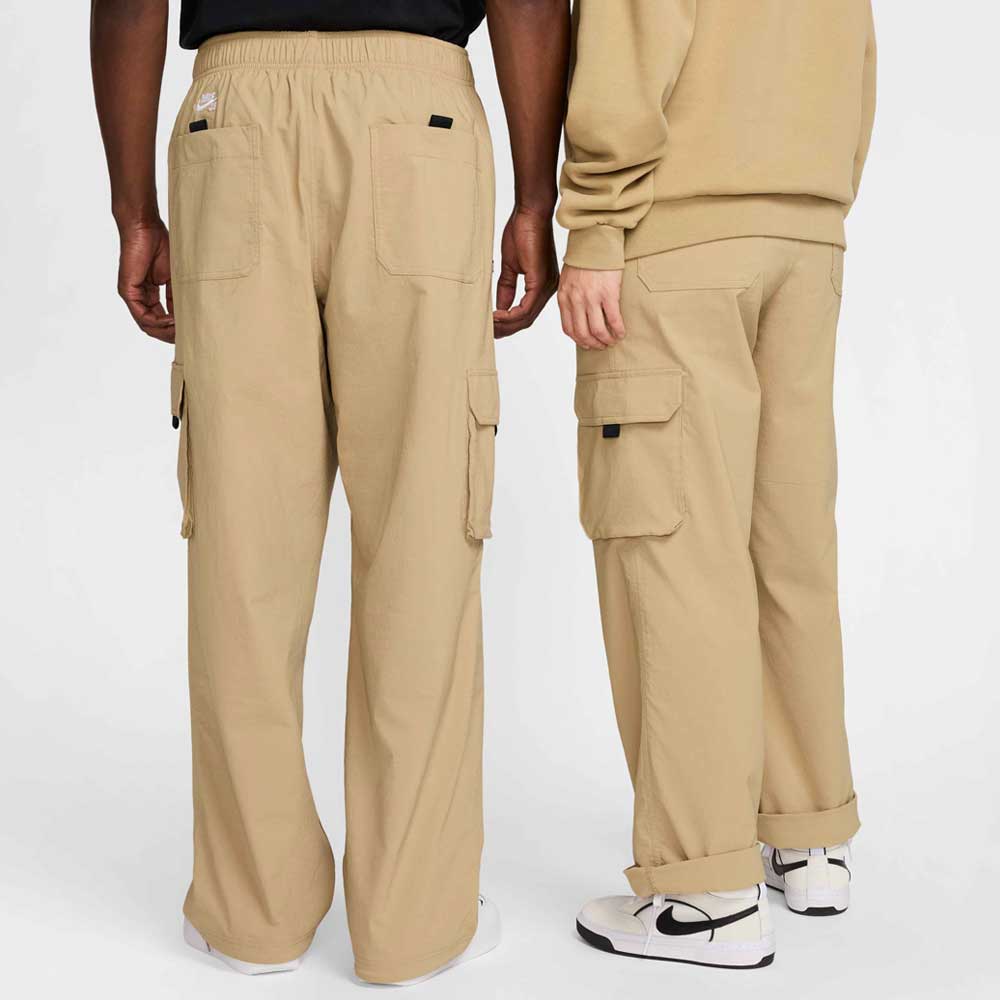 Two people wearing FV7347297 Kearny Cargo Pant Khaki Nike SB Skate Dri Fit stand side by side with their backs to the camera, highlighting the pants' large pockets and relaxed, skate-ready fit.