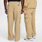 Two people wearing FV7347297 Kearny Cargo Pant Khaki Nike SB Skate Dri Fit stand side by side with their backs to the camera, highlighting the pants' large pockets and relaxed, skate-ready fit.