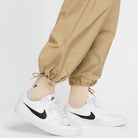 A person sports FV7347297 Kearny Cargo Pant Khaki Nike SB Skate Dri Fit, cream socks, and white Nike sneakers with black swooshes on a white background; only the lower legs and feet are visible in this classic skate-inspired look.