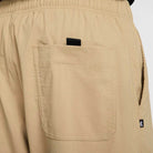 Close-up of the back pocket on the FV7347297 Kearny Cargo Pant Khaki Nike SB Skate Dri Fit, showing an elastic waistband, a black fabric loop above the pocket, and a small black tag with a white logo on the side seam.