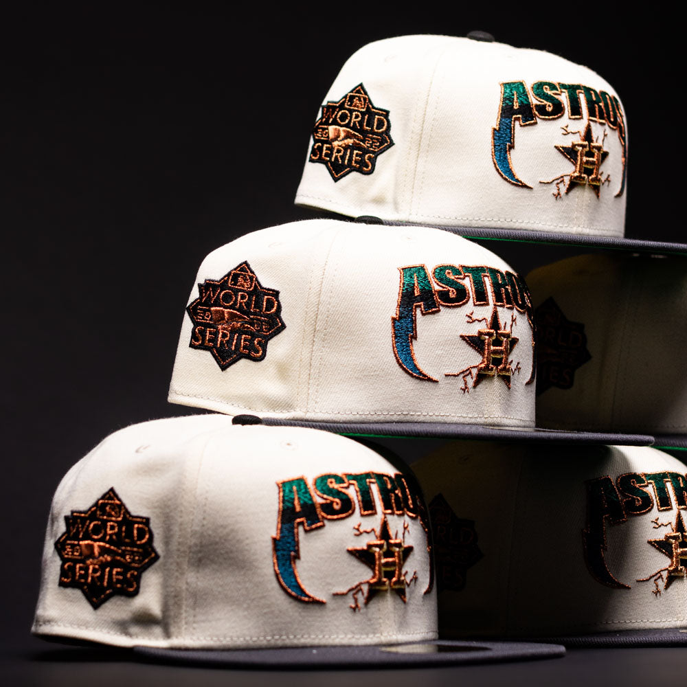 Four Undaground 22WS Chrome Houston Astros New Era Hat 5950 Fitted caps are stacked in a pyramid formation. Available at Chrome Undaground, these fitted hats showcase embroidered team logos and World Series patches, all set against a dark background with dramatic lighting emphasizing the intricate stitching details.