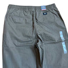 A pair of VN00000D1LE Range Baggy Tapered Taupe Pants from Vans Skateboarding is shown from the back, featuring two back pockets, an elastic waistband, plus brand tags near the waistband and along the side.