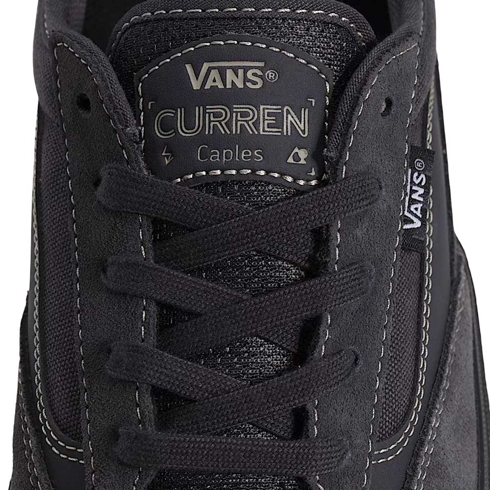 A close-up of the VN000D85CC81 Skate Curren Caples Charcoal Black Vans shows the tongue label, black laces, Vans logo tag, visible stitching, and suede material with durable Duracap underlays for added protection and longevity.