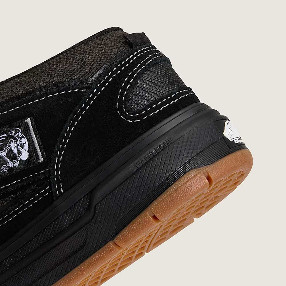 Close-up of the heel of the VN000D9ZKOU Black Asphalt Suede Skate Wafflecup Half Cab Vans shoe, featuring white stitching, a gum sole, visible Wafflecup label on the midsole, and a small white logo near the heel, showcasing its skate design.