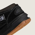 Close-up of the heel of the VN000D9ZKOU Black Asphalt Suede Skate Wafflecup Half Cab Vans shoe, featuring white stitching, a gum sole, visible Wafflecup label on the midsole, and a small white logo near the heel, showcasing its skate design.