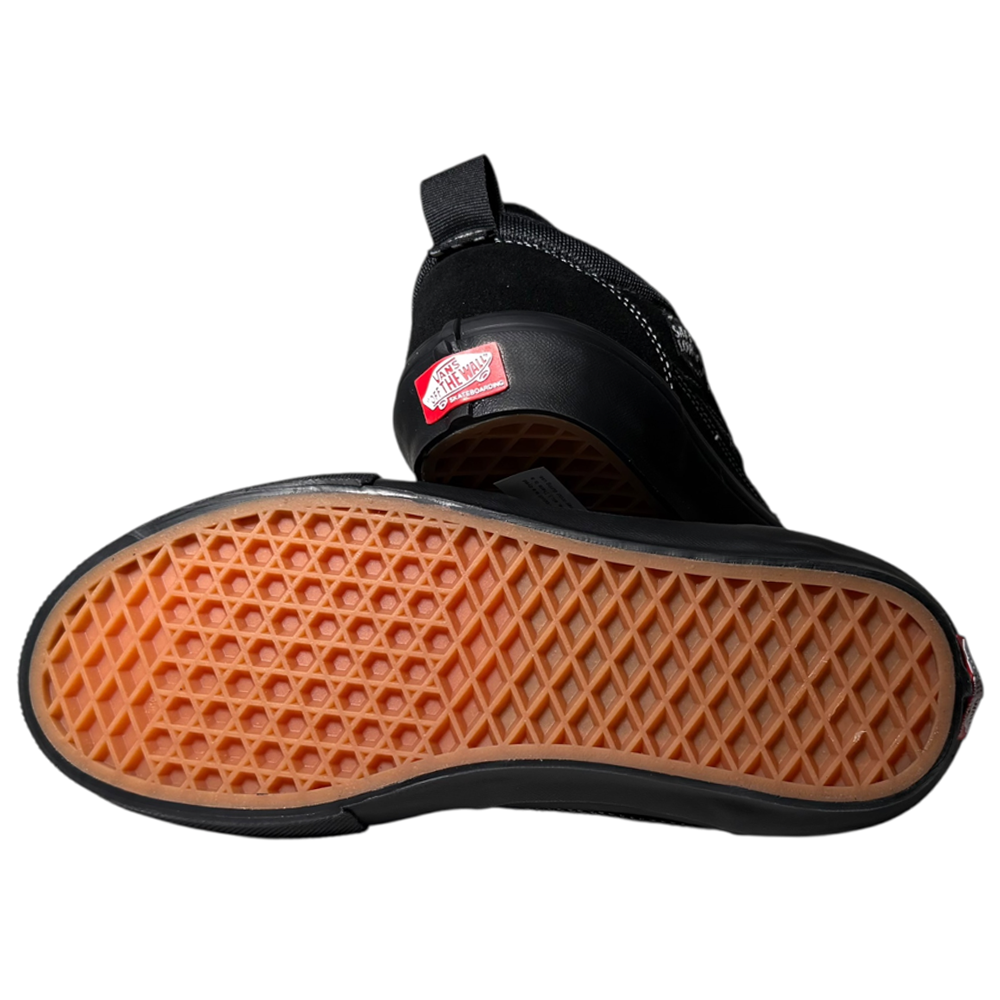 A pair of VN000EEHBKA1 Skate Safe Low Black Vans shoes—one flat to show the grippy, durable waffle sole, the other upright with the red Vans logo on the heel. Suede and rubber details highlight classic skate style.