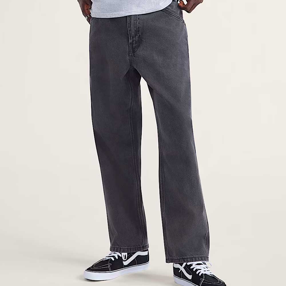 A person wears VN000KXMQ471 Skate Check 5 Loose Black Denim Vans Pants, paired with a light gray shirt and black-and-white sneakers, standing against a plain light background with only their lower body visible.