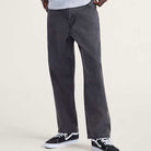 A person wears VN000KXMQ471 Skate Check 5 Loose Black Denim Vans Pants, paired with a light gray shirt and black-and-white sneakers, standing against a plain light background with only their lower body visible.