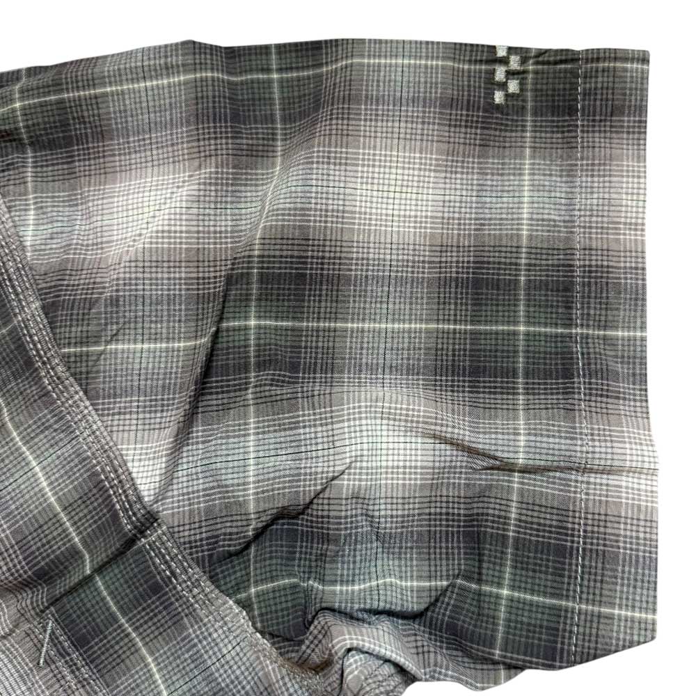 Close-up of the VN000KYW1NU1 Walnut Skate Plaid SS Woven Top Vans, featuring gray and white intersecting lines and a small white stitched cross in the upper right. The slightly wrinkled fabric echoes the classic Vans aesthetic.