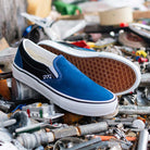 The VN0A2Z31Y40 Sport Blue Black Skate Slip On Vans Suede Shoes with white soles are displayed on a busy, tool-filled surface, emphasizing their durable design for skateboarding.