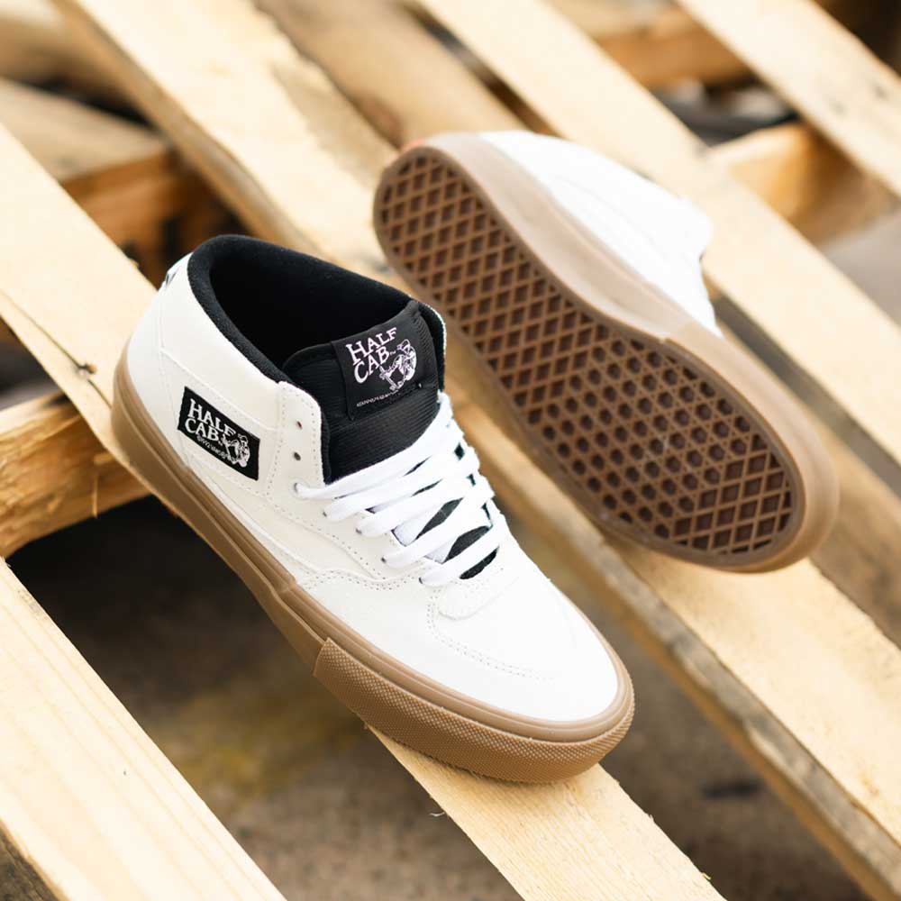A pair of VN0A2Z348YG Antique White Gum Suede Skate Half Cab Vans Shoes featuring PopCush footbeds, brown gum soles, and black tongue tags sits on a wooden pallet.