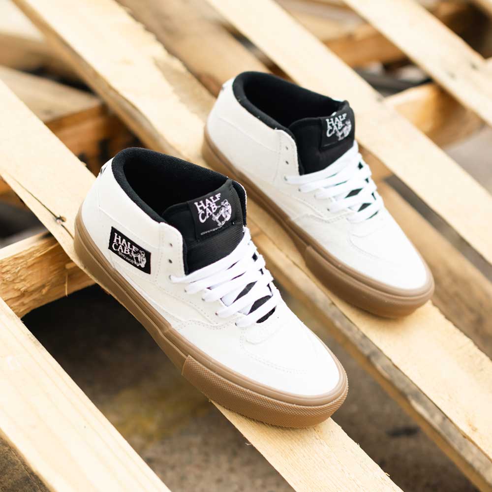 A pair of VN0A2Z348YG Antique White Gum Suede Skate Half Cab Vans Shoes with brown soles and black accents are placed on a wooden pallet outdoors.