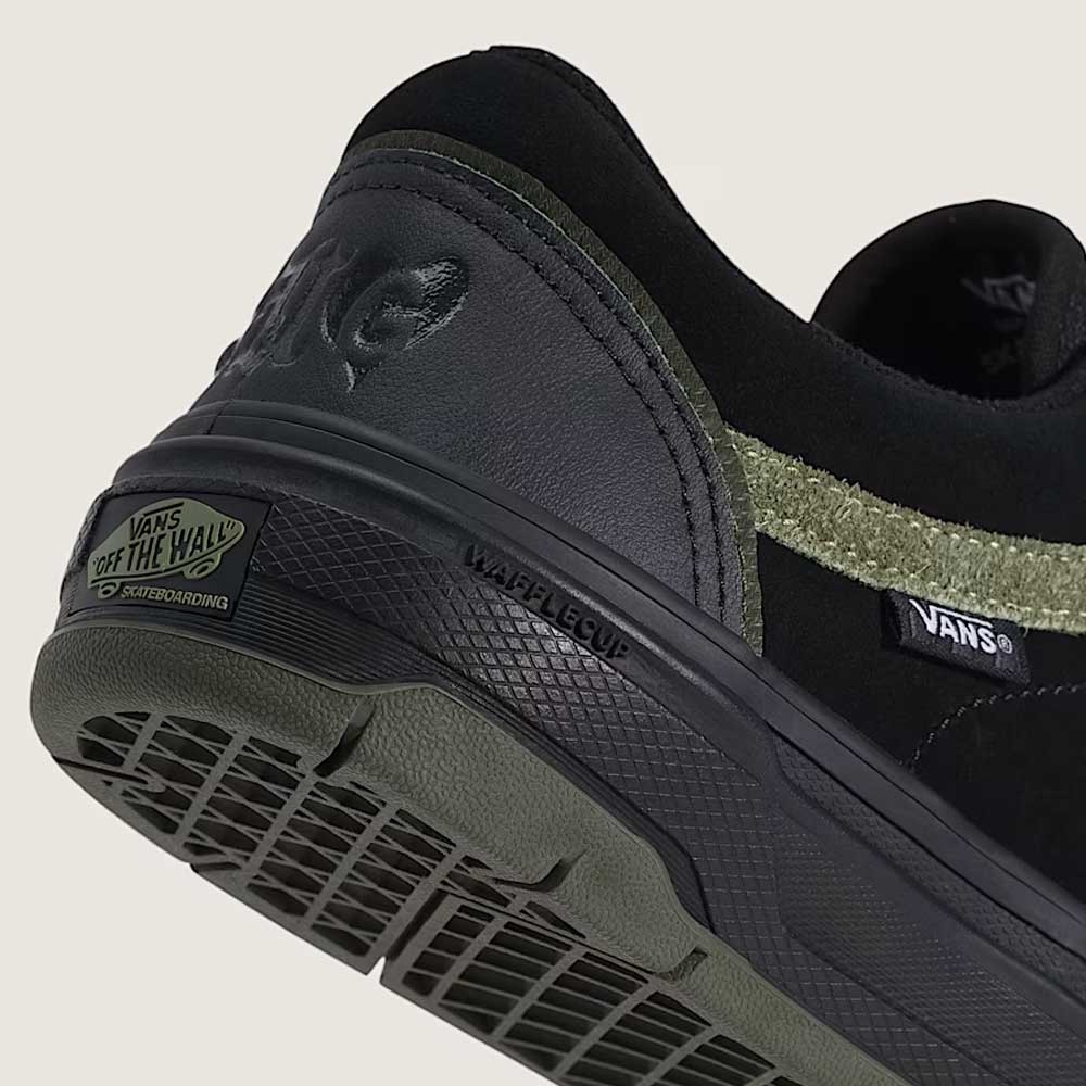 Close-up of Vans Skate Half Cab Walnut Gum VN0A5FCD77J1 suede skateboard shoes in black, featuring a textured green stripe, PopCush impact protection, WAFFLECUP sole, and "Off The Wall" heel label against a plain background. Perfect for skateboarding.