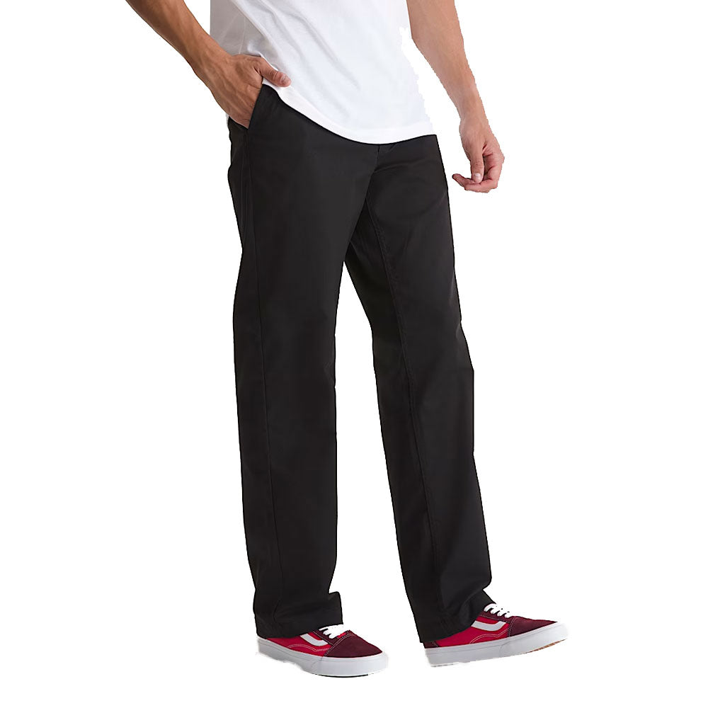 Wearing Vans Straight Chino Black VN000TCXBLK1 Skate Check 5 Pants, a white t-shirt, and red sneakers with white soles, a person stands with one hand in their pocket against a plain white background.