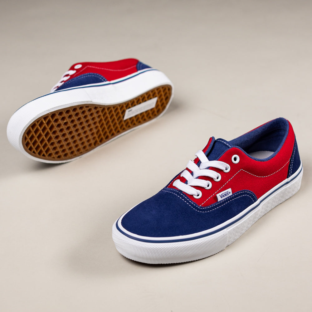 The Skate Era Blue Red VN000ECR3QG1 Vans feature red and navy blue suede uppers, white laces, and white rubber soles. Display includes one upright shoe and one on its side to show off the signature waffle-patterned grip.