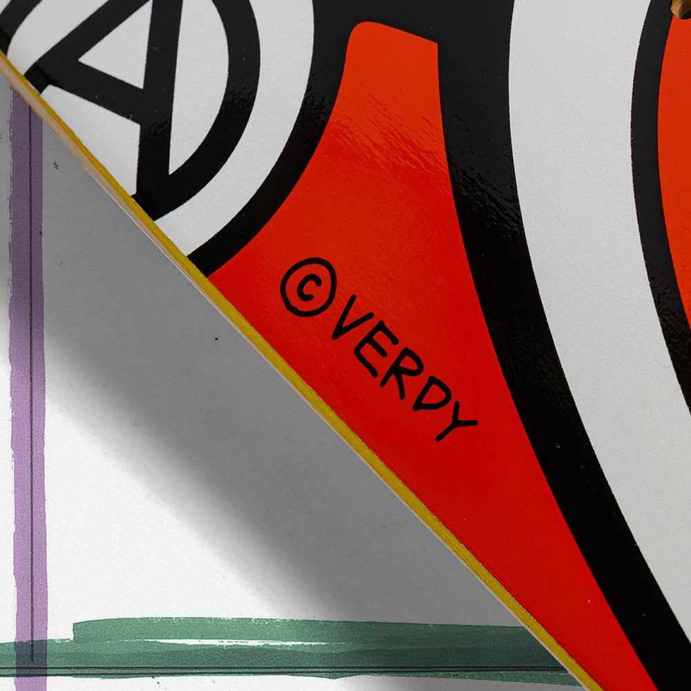 Close-up of two overlapping skateboards with bold graphic designs and vivid colors. The bottom one is the Verdy Oval 8.38 Real Skateboard Deck Skateshop Day, featuring ©VERDY in black on a red and white background.