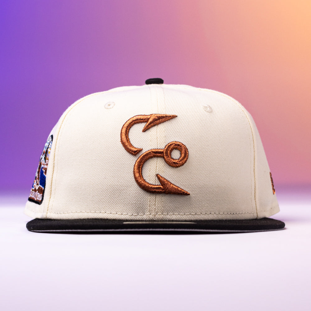 Introducing the Warren 2.0 Hooks Chrome Black New Era Hat 5950 Fitted: this cream-colored hat features a black brim and showcases two brown embroidered fish hooks on the front, set against a vibrant gradient of purple, pink, and orange—a bold Chrome Black finish in the iconic 5950 Fitted style.