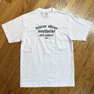 The White Divine Shine x Southside Still Holdin Max Heavyweight Tee features embroidered Southside Skatepark style, laid flat on a wooden floor with black gothic “divine shine. southside still holdin’ 1994” text.