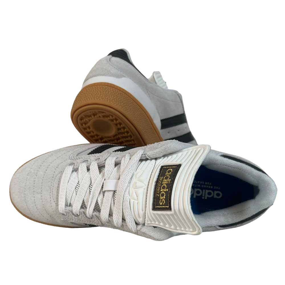 A pair of White Grey Shaoli Gum Busenitz Adidas Skateboarding Suede Shoes—one on its side, the other upright—features black stripes, Adidas logo on the tongue, and a blue insole.