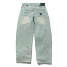 The Wide Cut Tinted Blue Wash Denim Jeans from Butter Goods feature a light blue wash, two back pockets, a subtly faded look, green belt loops, and a black patch above the right pocket. They offer a relaxed fit and wide cut style.