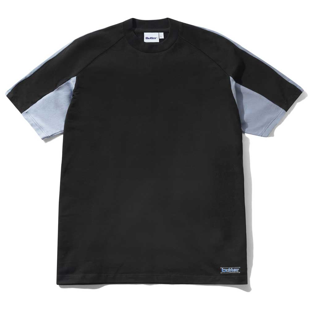 The Butter Goods Worldwide Panelled Tee in Black features light gray sleeve panels and a black torso, shown laid flat with a small rectangular label near the bottom hem.