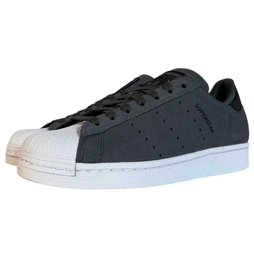 The Superstar ADV Adidas Grey Black Suede Shoes feature a dark gray low-top design with white rubber shell toes, white soles, black laces, SUPERSTAR on the side, and subtle reflective badging for added style.