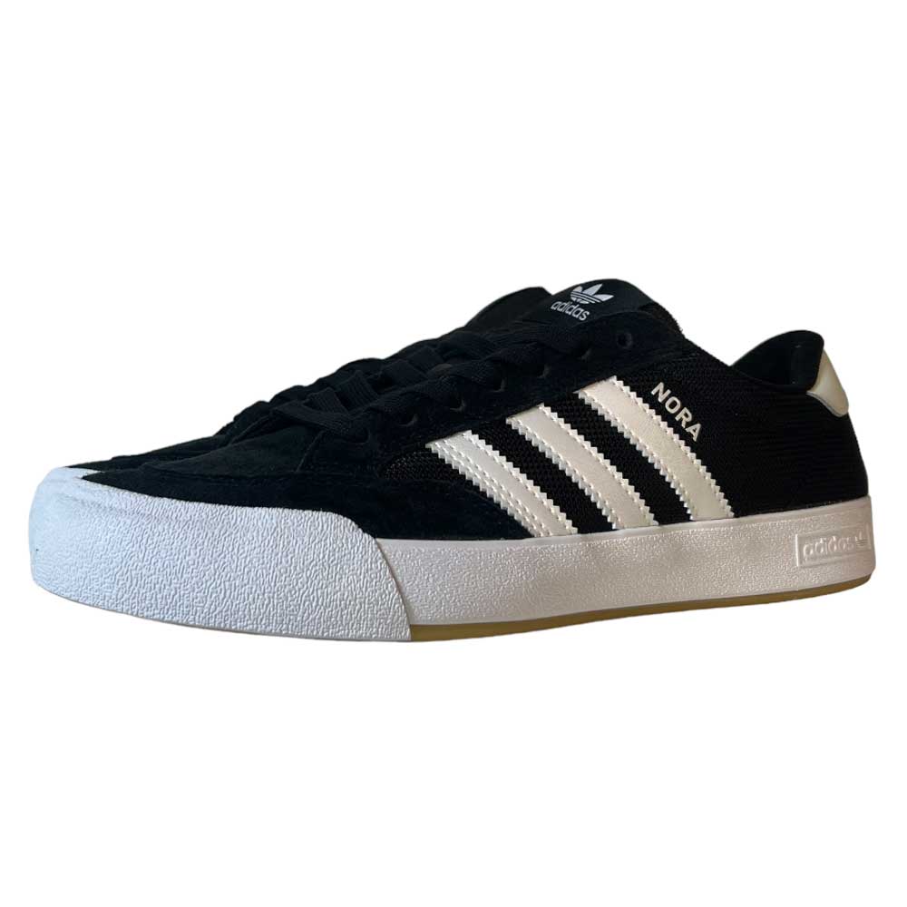 The Adidas Nora Black Zero Spark Suede Knit Shoes feature black suede with white stripes, a white sole, and "NORA" in gold on the side as a tribute to Nora Vasconcellos, displayed angled to show the outer side and front.