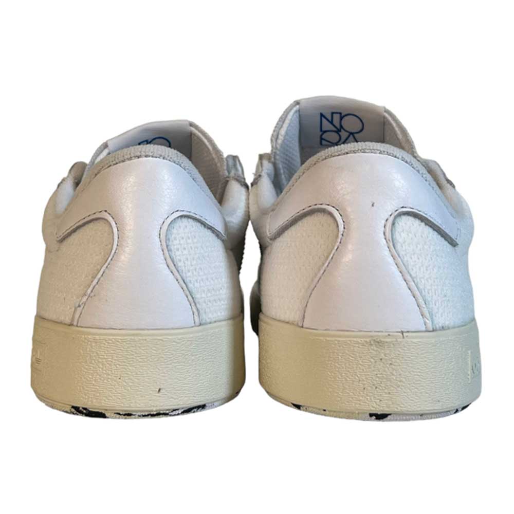 The Adidas Skateboarding Nora White White Leather Knit Shoes are shown from the back, with textured details, off-white rubber soles, and blue text on the inner lining. The vintage-inspired shoes are placed side by side on a white background.
