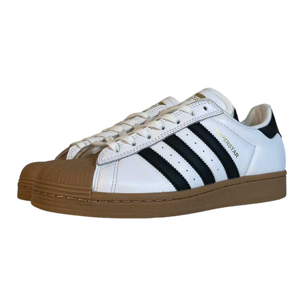 The Adidas Superstar ADV White Black Gum Leather Shoes feature white leather uppers, black stripes, gold "Superstar" text, and brown rubber shell toes and soles, displayed on a white background.