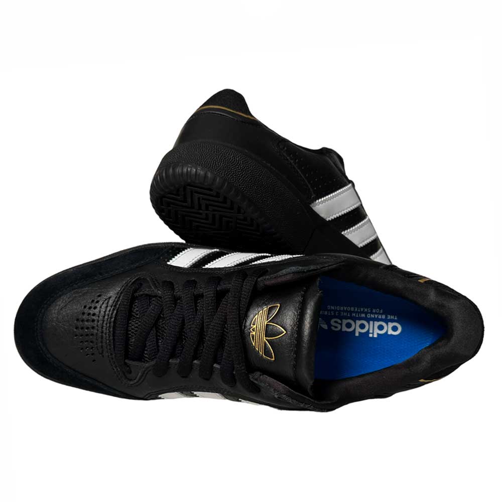 A pair of Tyshawn Low Adidas Skateboarding Black White Leather Suede Shoes, featuring white stripes and gold accents, is shown from top and side views. The blue insole displays white Adidas branding.