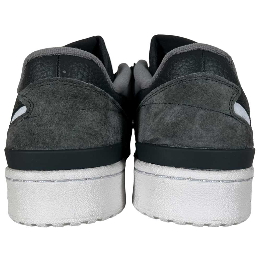 A rear view of the Forum 84 Low Adidas Skateboarding Carbon White Gray Leather Shoes, featuring dark gray suede, black and white accents, white textured soles, and padded gray collars inspired by the classic Forum 84 Low design.