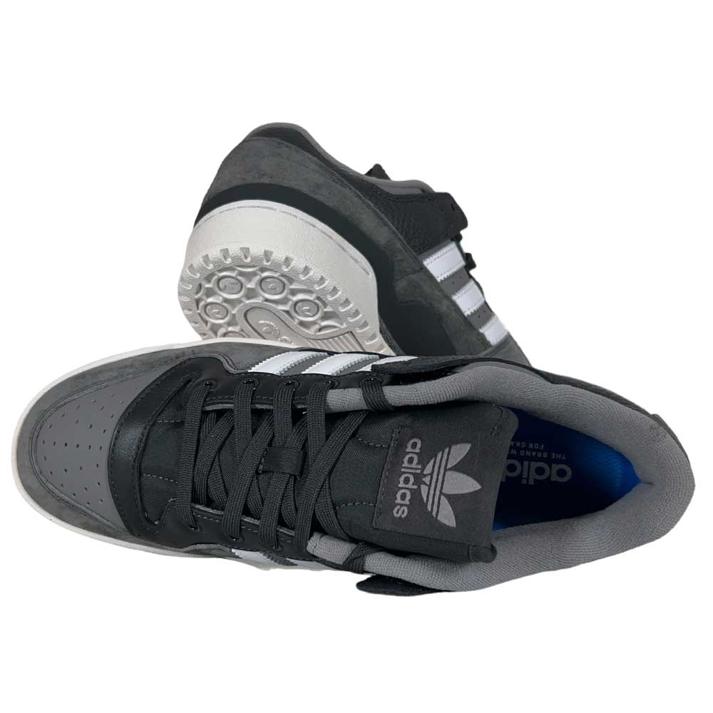 A pair of Forum 84 Low Adidas Skateboarding Carbon White Gray Leather Shoes—one stands upright showing side and sole, the other is on its side displaying the Adidas logo on the tongue.