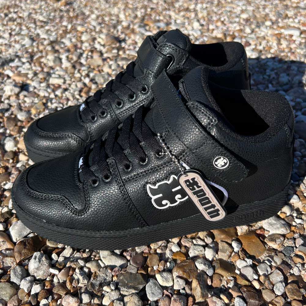 A pair of Grasshopper Black Leather I Path Shoes with textured pebble grain leather and lace-up fronts are placed on a pebbled surface, featuring a puzzle piece logo and a tag reading "Autism.