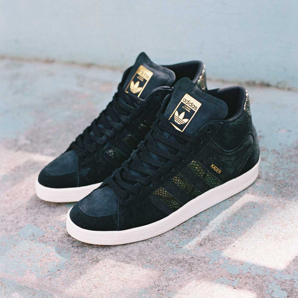The Superskate x Kader Shoes (JQ4413) are black Adidas skateboarding shoes with suede and leather upper, off-white soles, and gold accents, shown on a concrete surface.
