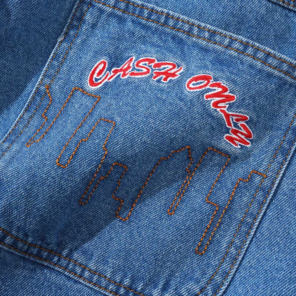 Close-up of the Logo Baggy Denim Jeans Washed Indigo Cash Only pocket, featuring orange-stitched city skyline outlines and "CASH ONLY" in bold red and white lettering above the design.