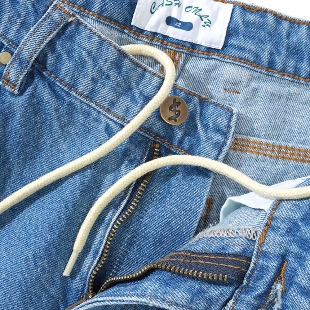 Close-up of Logo Baggy Denim Jeans Washed Indigo Cash Only, featuring a white drawstring, visible zipper, metal button, and a white label on the waistband displaying “Casa Mazc” and size “32.”.