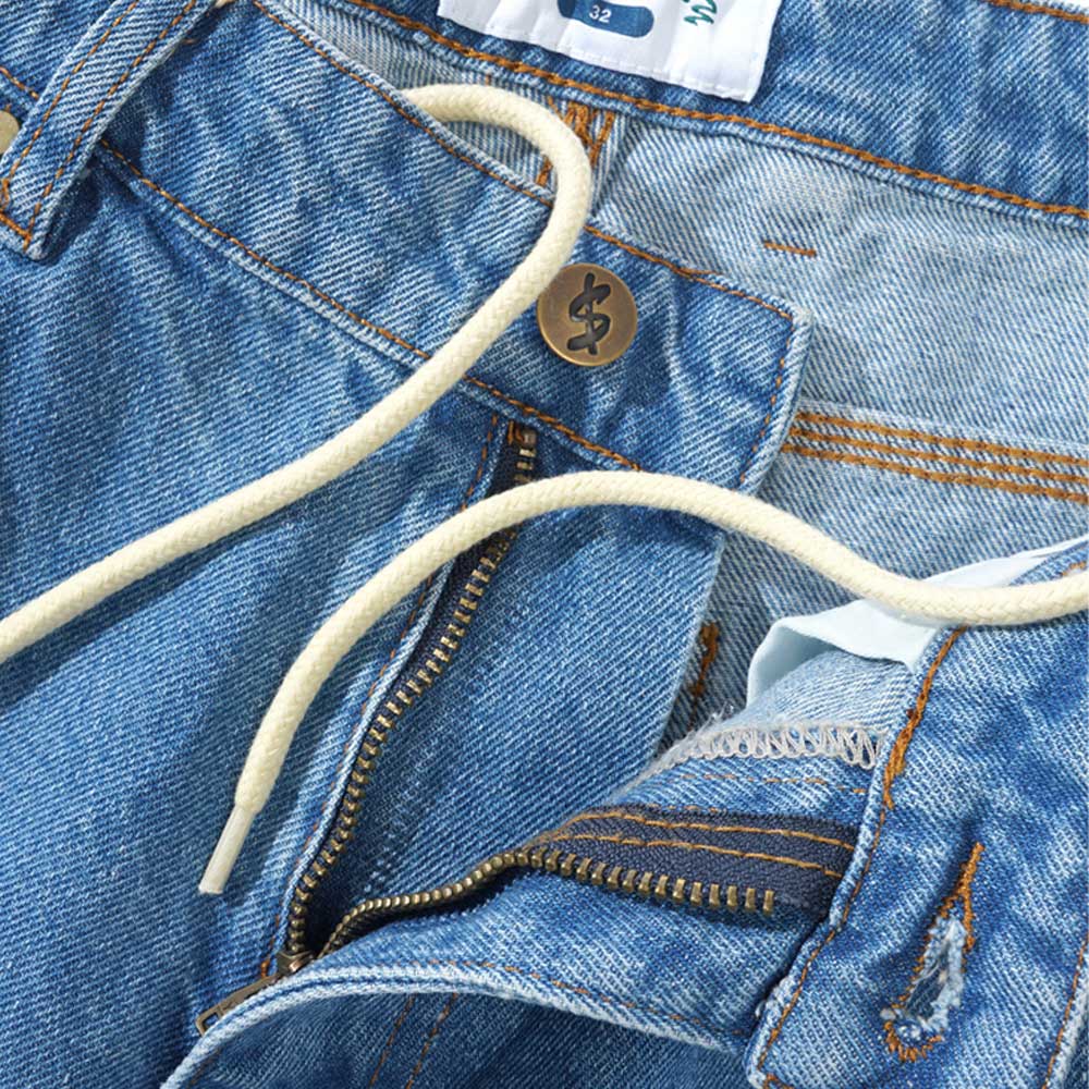 A close-up of the Logo Baggy Denim Shorts Washed Indigo Cash Only, showing baggy fit, white drawstring, brass button, partially unzipped fly, stitching details, and part of the waistband label.