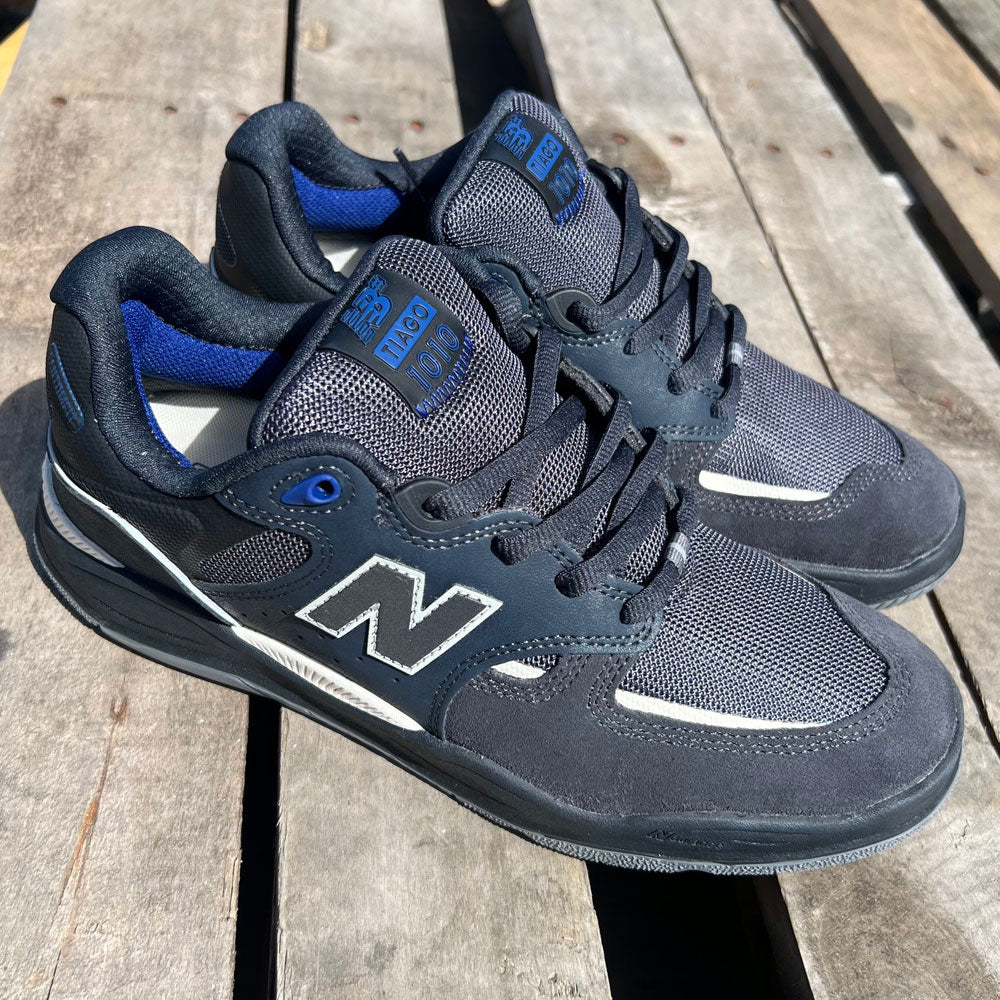 A pair of navy and white 1010 UR New Balance Numeric Tiago Lemos suede shoes with mesh panels, side by side on a wooden pallet in sunlight.