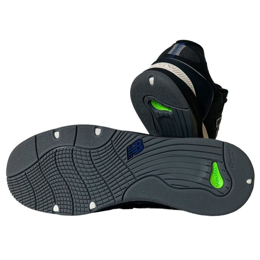 A pair of New Balance Numeric 1010 UR Tiago Lemos Suede Shoes in navy and white, shown from the bottom to highlight the textured gray soles with green and white accents and the blue New Balance logo—crafted for performance.