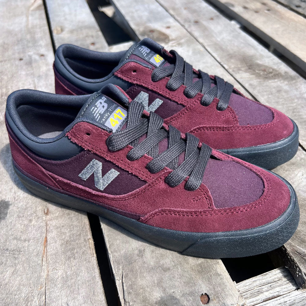 A pair of 417 WBP New Balance Numeric Franky Villani Eggplant Black Suede Skateboarding Shoes with black laces and soles, shown on a weathered wooden surface in sunlight.