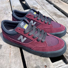 A pair of 417 WBP New Balance Numeric Franky Villani Eggplant Black Suede Skateboarding Shoes with black laces and soles, shown on a weathered wooden surface in sunlight.