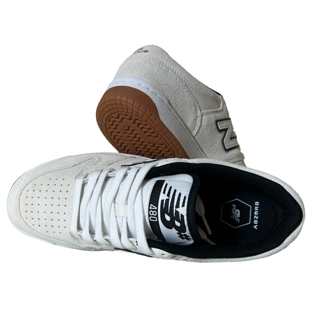 A pair of 480 SWG New Balance Numeric Shoes in suede white/black; one stands upright showing laces, the other angles to reveal the brown sole, both featuring the classic New Balance logo.