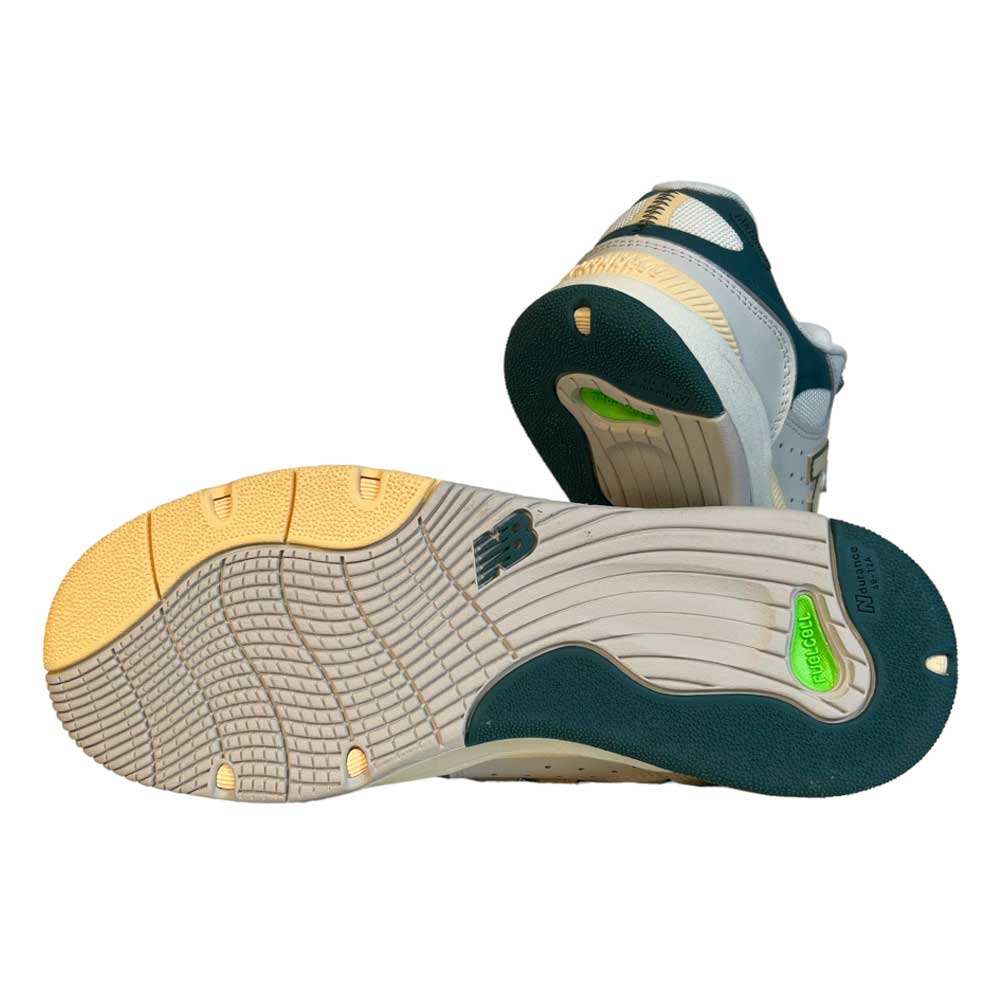 The 1010 AL New Balance Numeric Suede Shoes in white, green, and yellow feature textured rubber soles with branding and traction patterns inspired by pro skater Tiago Lemos, shown from the bottom for a close-up view.